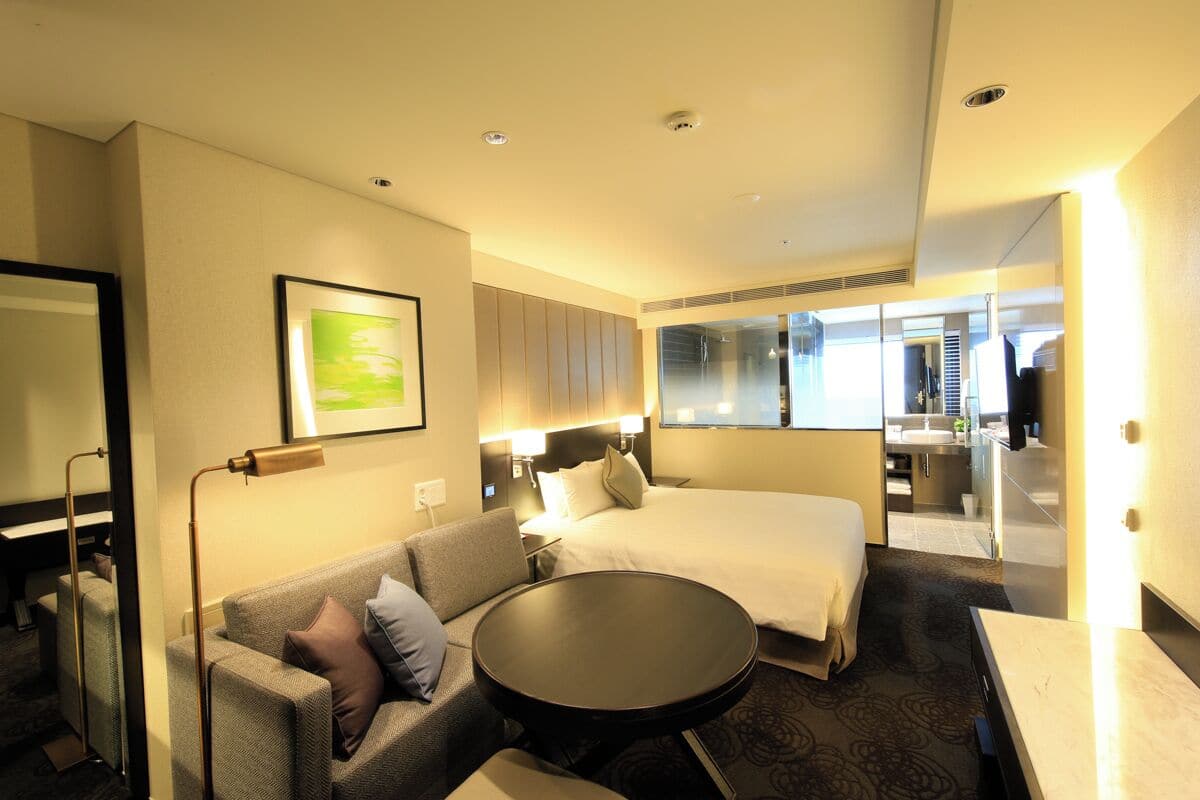 Habitación de hotel con cama, sofá, una mesa redonda, un espejo y vista al baño.