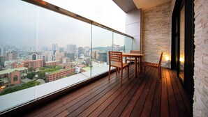 Un balcón con piso de madera, una mesa y sillas. Se aprecia una vista de la ciudad con edificios e iglesia.