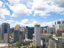 Paisagem urbana com edifícios modernos altos, uma torre imponente com design único, e um céu azul límpido com nuvens esparsas.