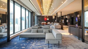 Un vestíbulo moderno de hotel con un sofá modular grande, un mostrador de recepción y grandes ventanales con vistas a la ciudad.