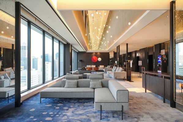 A modern hotel lobby with a large sectional sofa, a reception desk, and large windows offering city views.