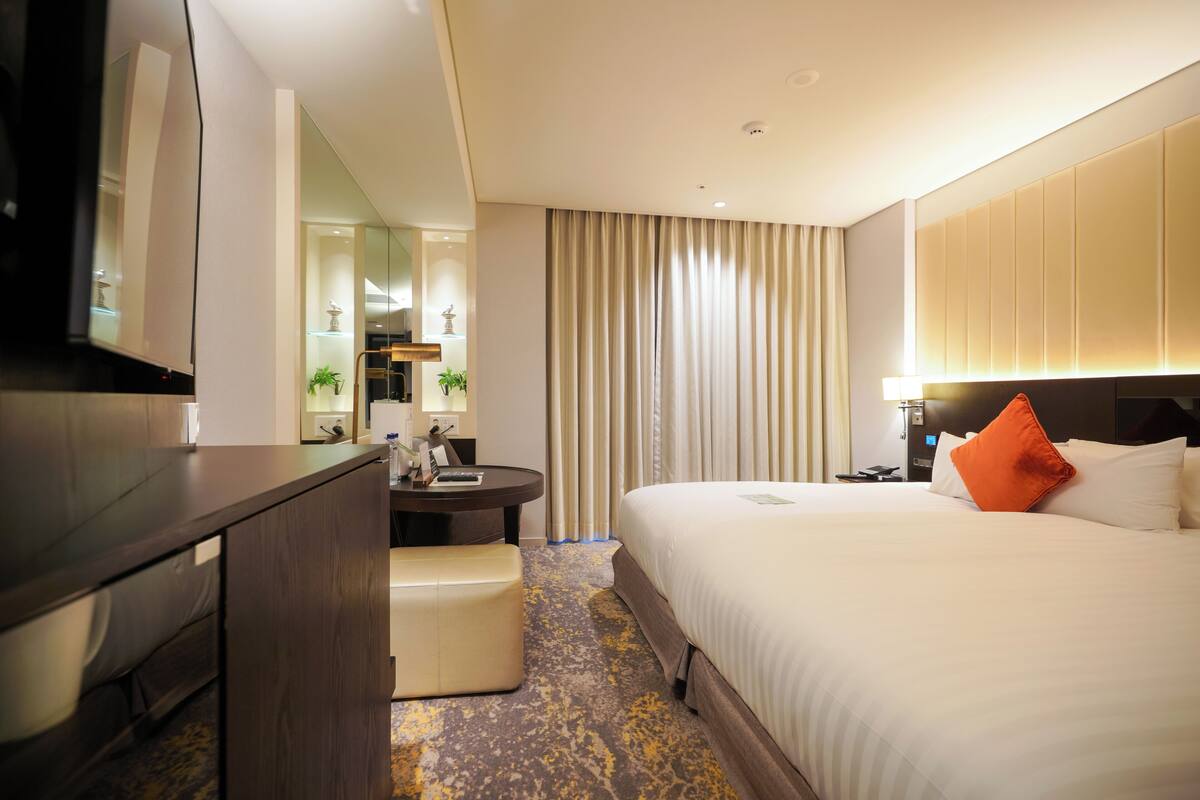 Habitación de hotel con cama, escritorio, silla, televisor y baño.