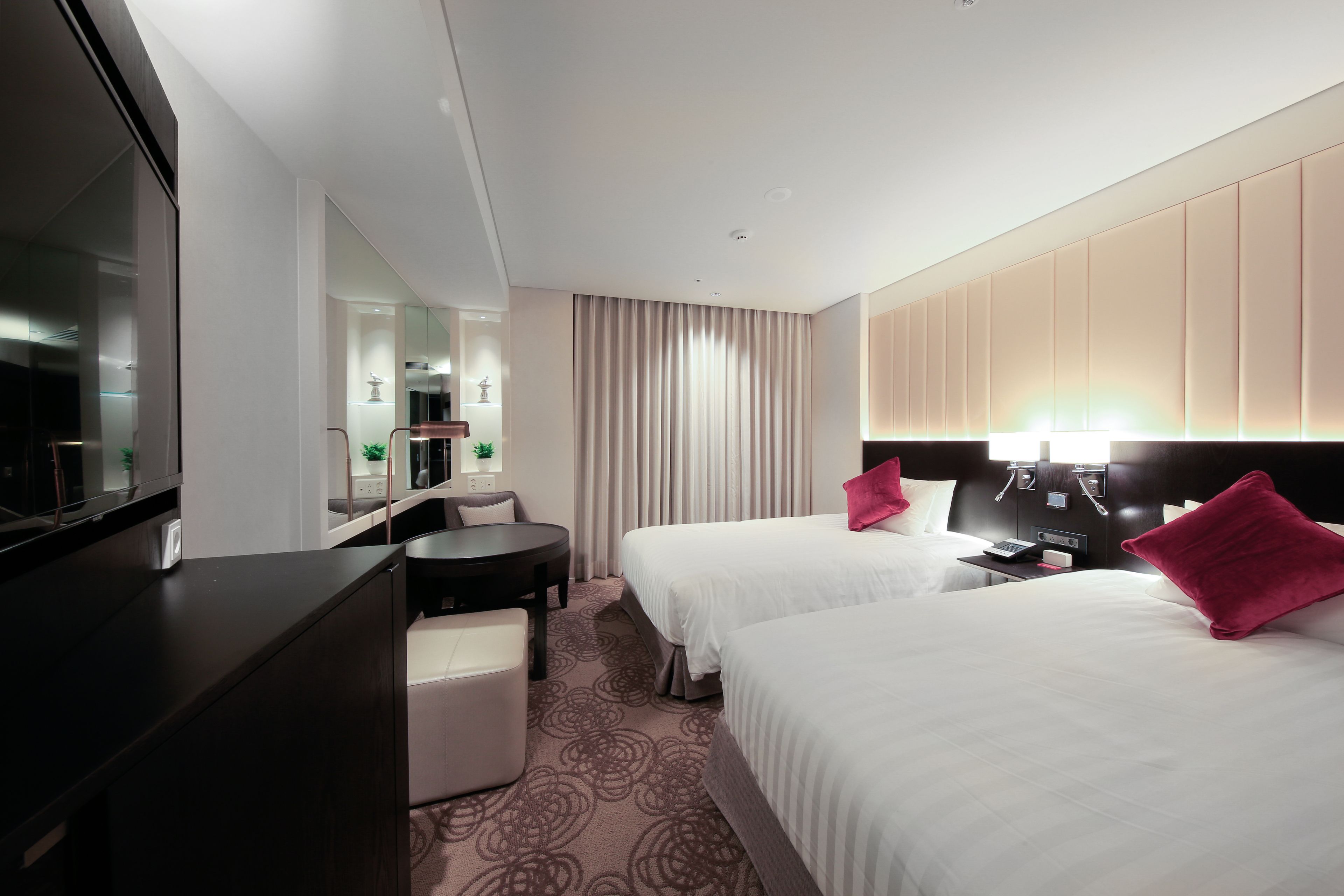 A hotel room with two beds, a desk, a chair, a TV, and a mirror.