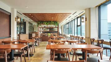A spacious restaurant with wooden tables and chairs, a central bar area, and large windows offering views of the city.