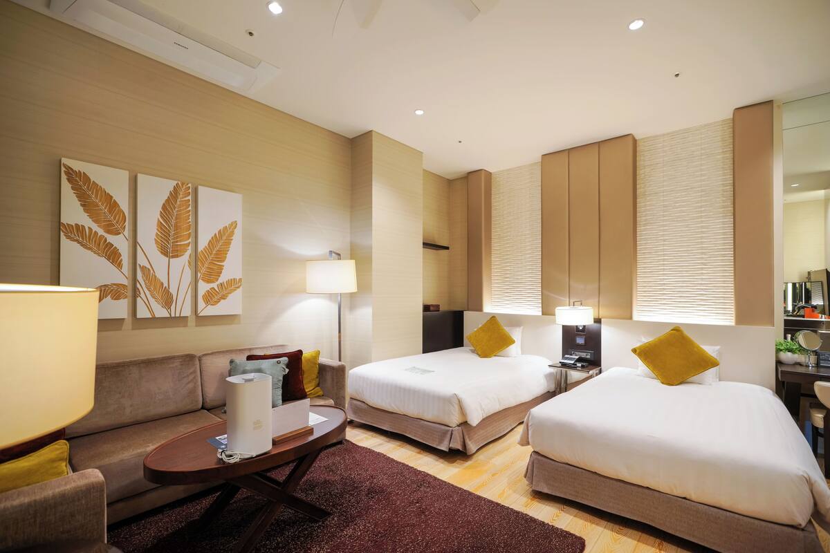 Habitación de hotel con dos camas, un sofá, un escritorio y una lámpara.
