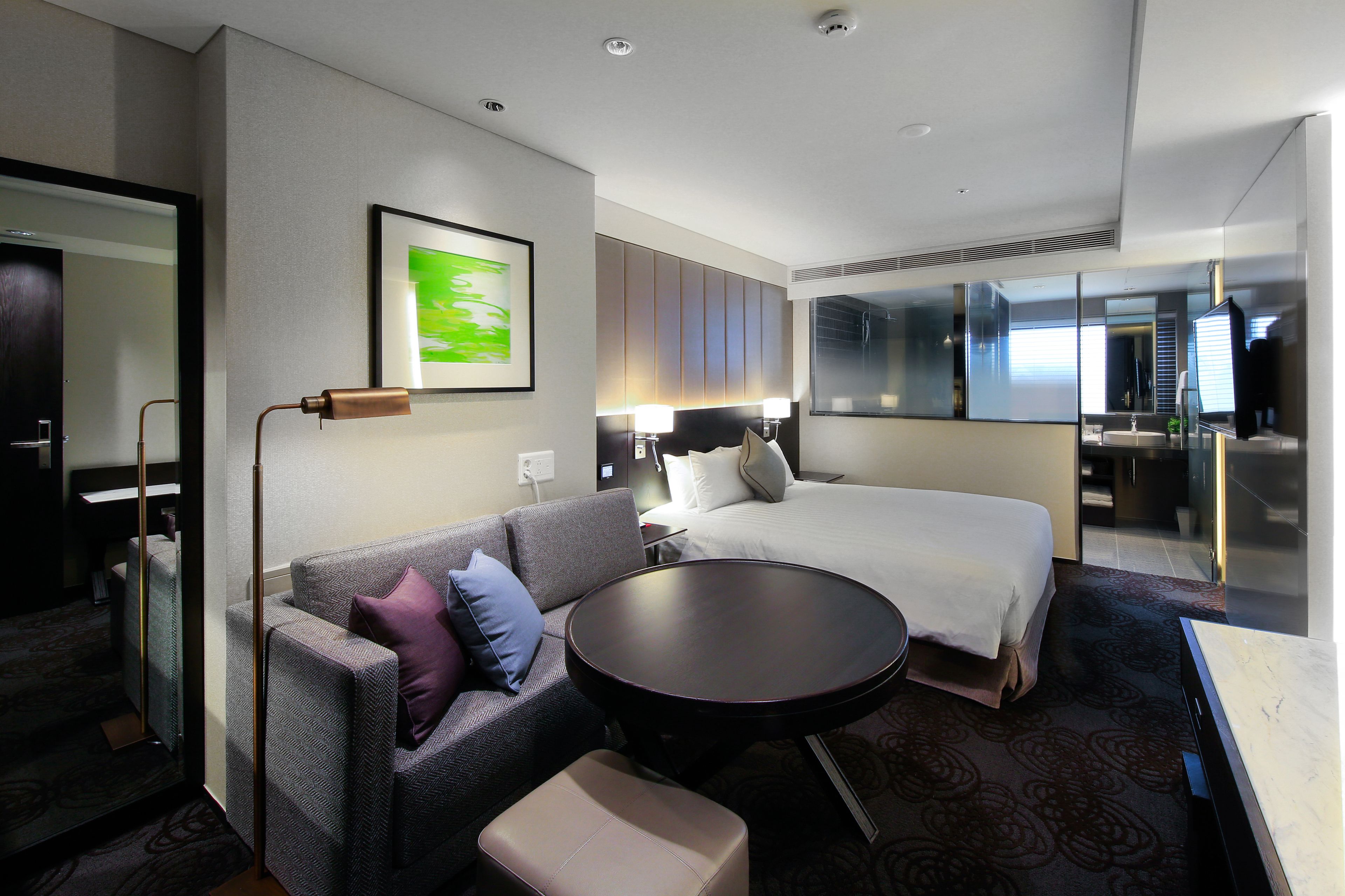 A hotel room with a bed, a sofa, a small table, and a large mirror.