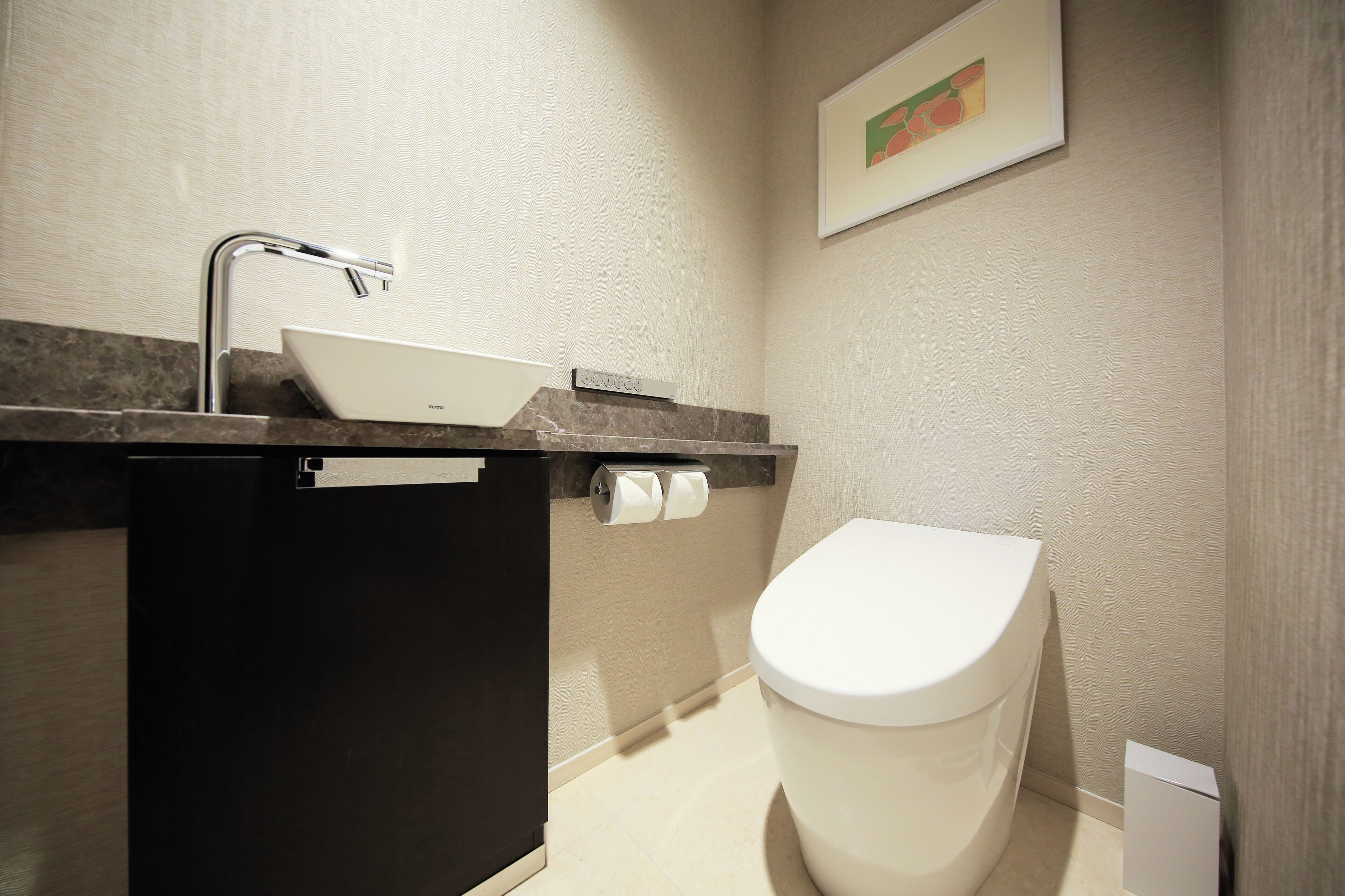 A modern bathroom with a white sink, a black cabinet, a toilet, and a framed picture on the wall.