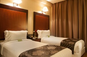 Habitación de hotel con dos camas, una mesita de noche con lámpara, un espejo y una ventana con cortinas.