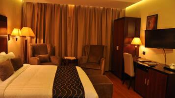 Quarto de hotel com uma cama grande, duas poltronas, uma mesa de trabalho e uma divisória.