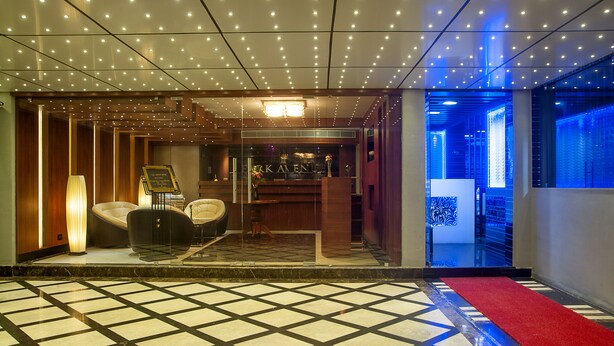 Un vestíbulo de hotel con piso a cuadros, alfombra roja y un área de descanso con lámpara y sillones.