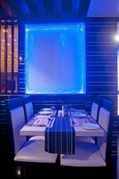 Un área de comedor con una mesa dispuesta para dos personas, con manteles individuales a rayas y sillas blancas.