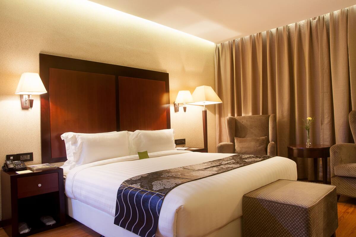 Ein Hotelzimmer mit einem großen Bett, zwei Nachttischlampen, einem Nachttisch, einem Sessel und einem kleinen Tisch mit einer Vase.
