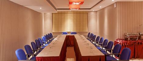 Un salón de conferencias con una larga mesa, sillas azules y un mantel rojo.