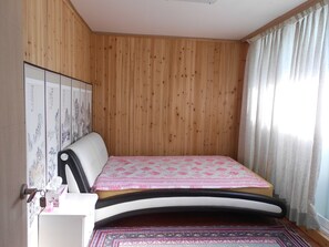 Une pièce aux murs recouverts de lambris en bois, un lit avec une couvre-lit à motifs, une table de chevet avec une boîte à mouchoirs et un tapis décoratif.
