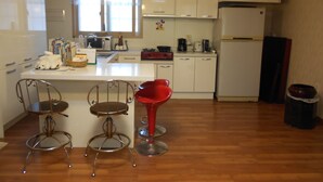 Une cuisine avec des meubles blancs, un réfrigérateur, un four à micro-ondes et un évier. On y trouve deux tabourets de bar rouges et un tabouret de bar en métal.