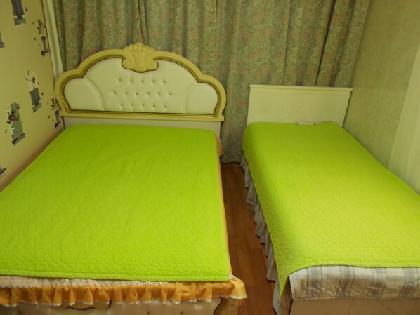 Une chambre avec deux lits, chacun recouvert d’une couverture verte et doté d’une tête de lit blanche.