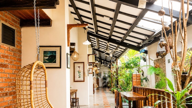 A restaurant with a hanging chair, wooden tables, chairs, and potted plants. - Palm Mansion Boutique Suites (George Town)