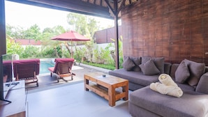 Area salotto esterna coperta con piscina, mobili in legno e un divano con un asciugamano.