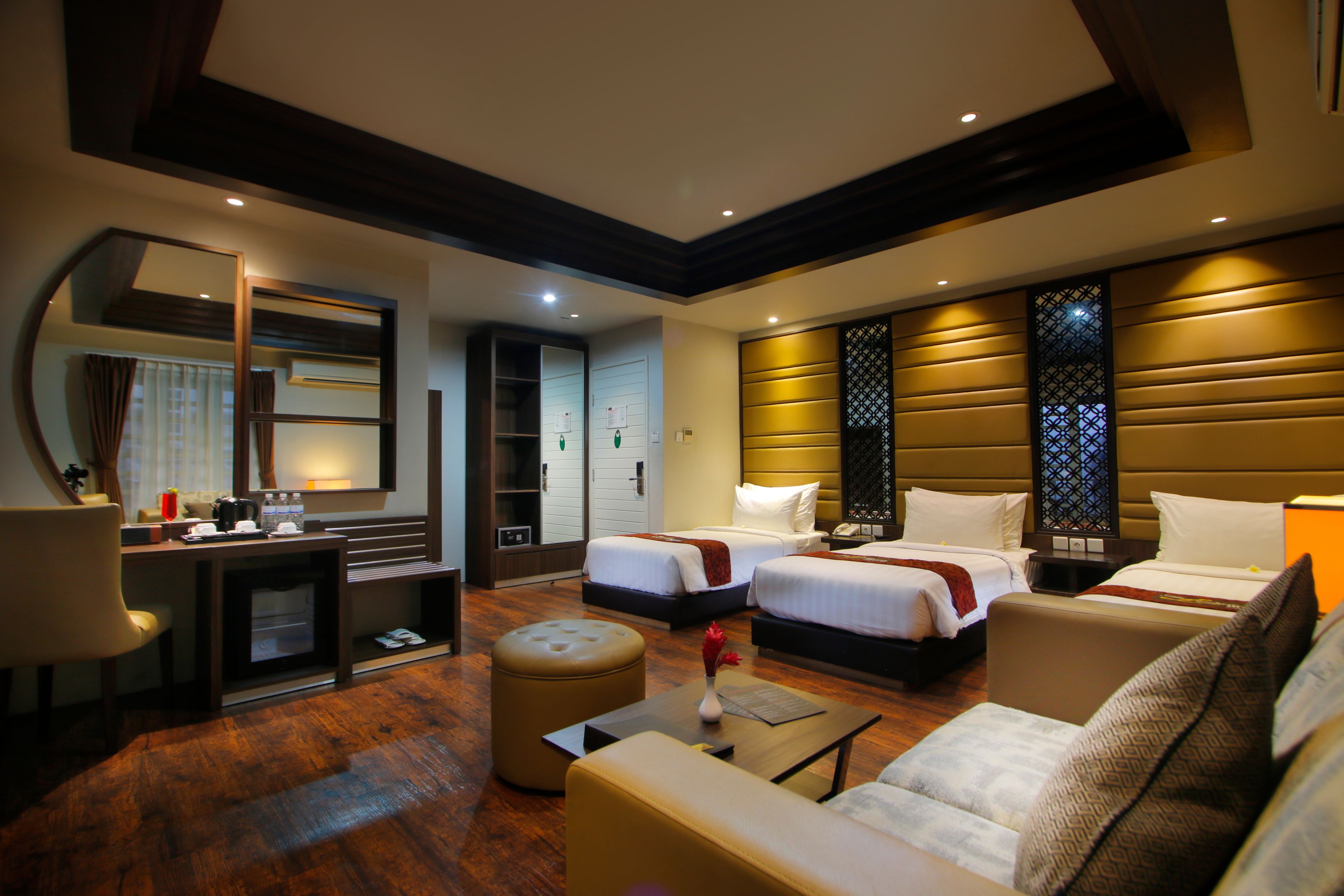 A hotel room with two beds, a sofa, a coffee table, a desk, and a mirror.