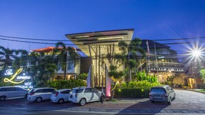 A modern hotel with a prominent neon sign, a covered outdoor area, and parked cars. - The Lerina Hotel Nusa Dua (Nusa Dua)