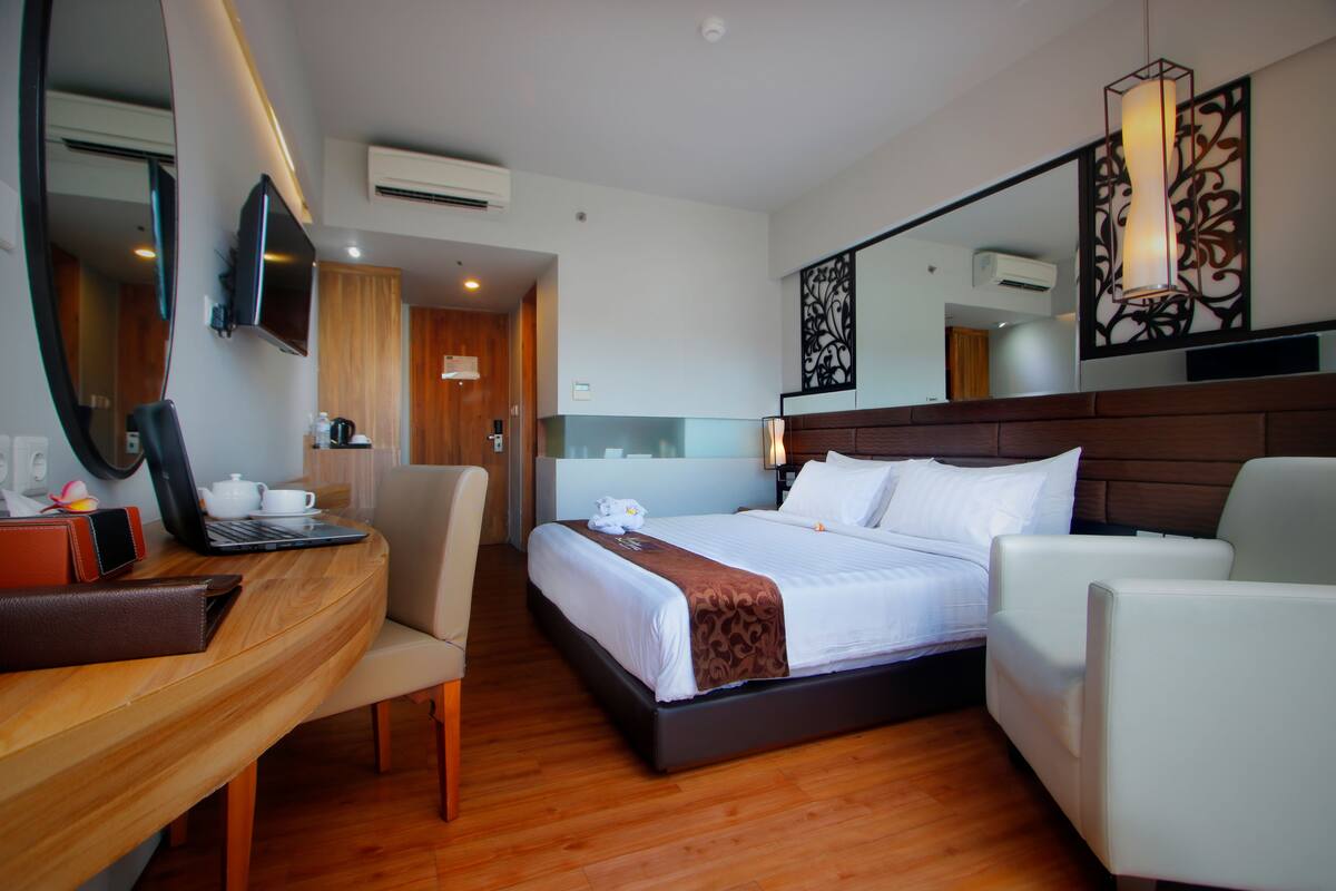 Una habitación de hotel con cama, escritorio, silla, televisor y espejo.