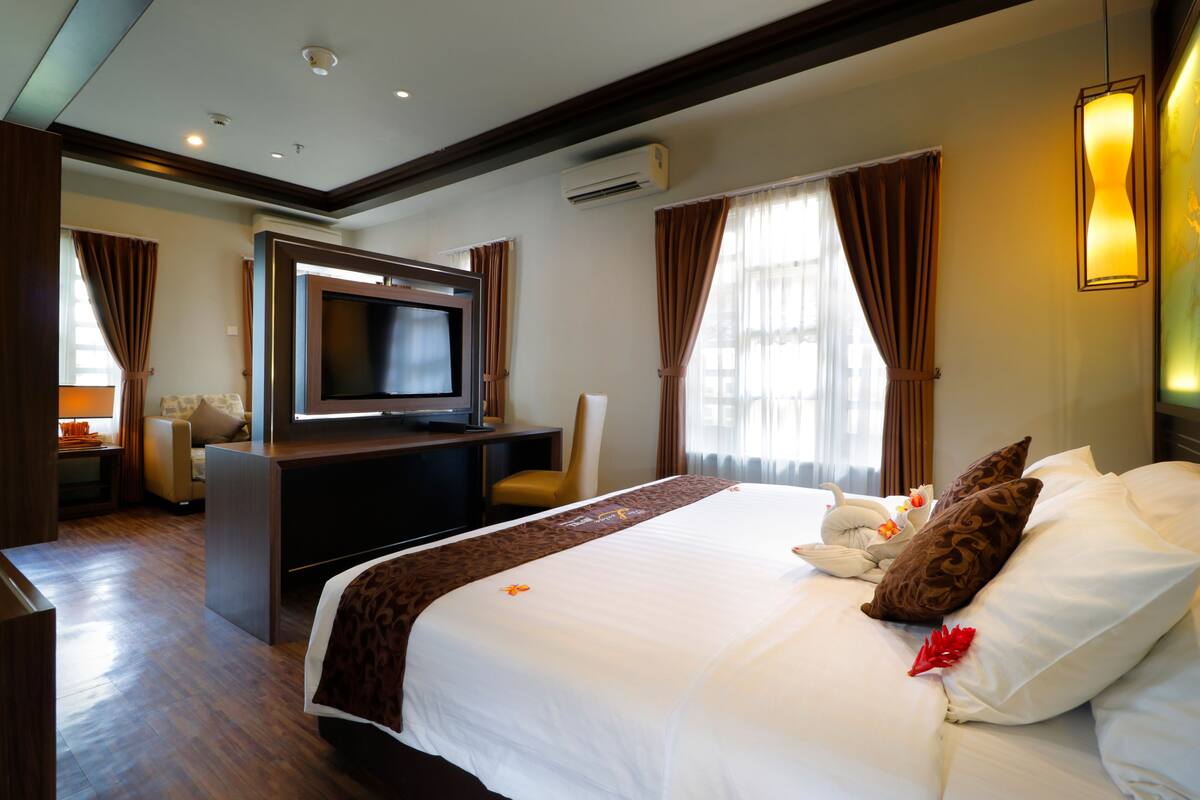 Una habitación de hotel con una cama grande, un escritorio con televisión de pantalla plana, una silla y un sofá.