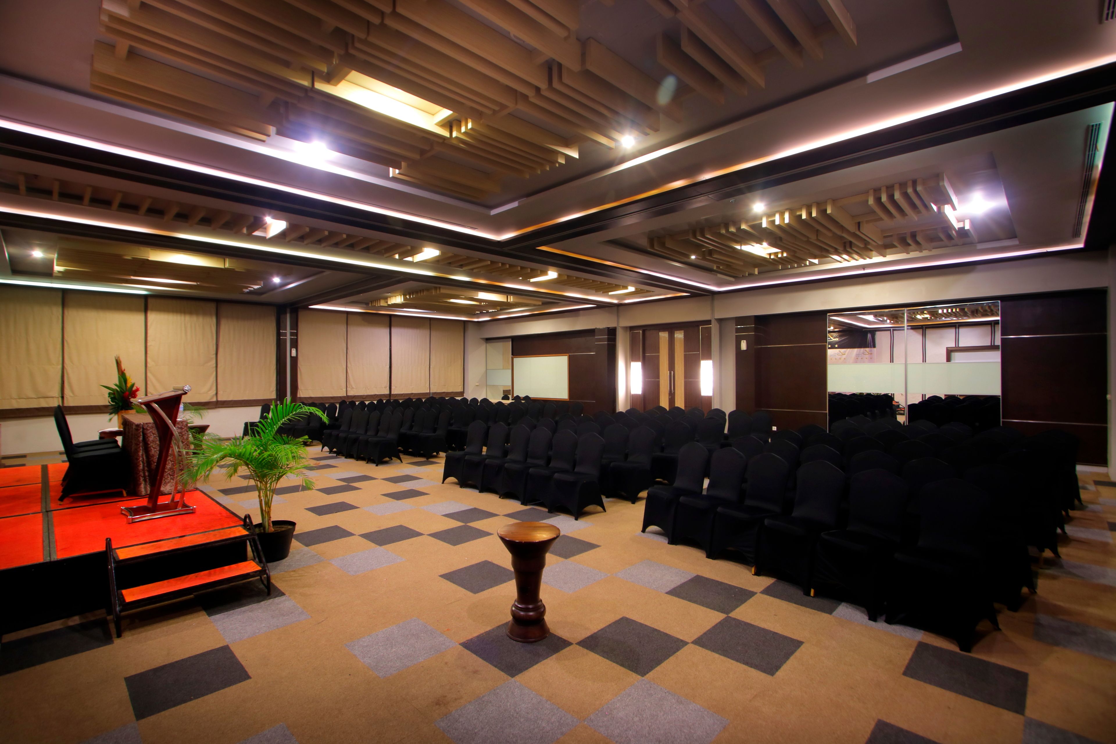 A conference room with rows of black chairs, a stage with a podium, and a potted plant.