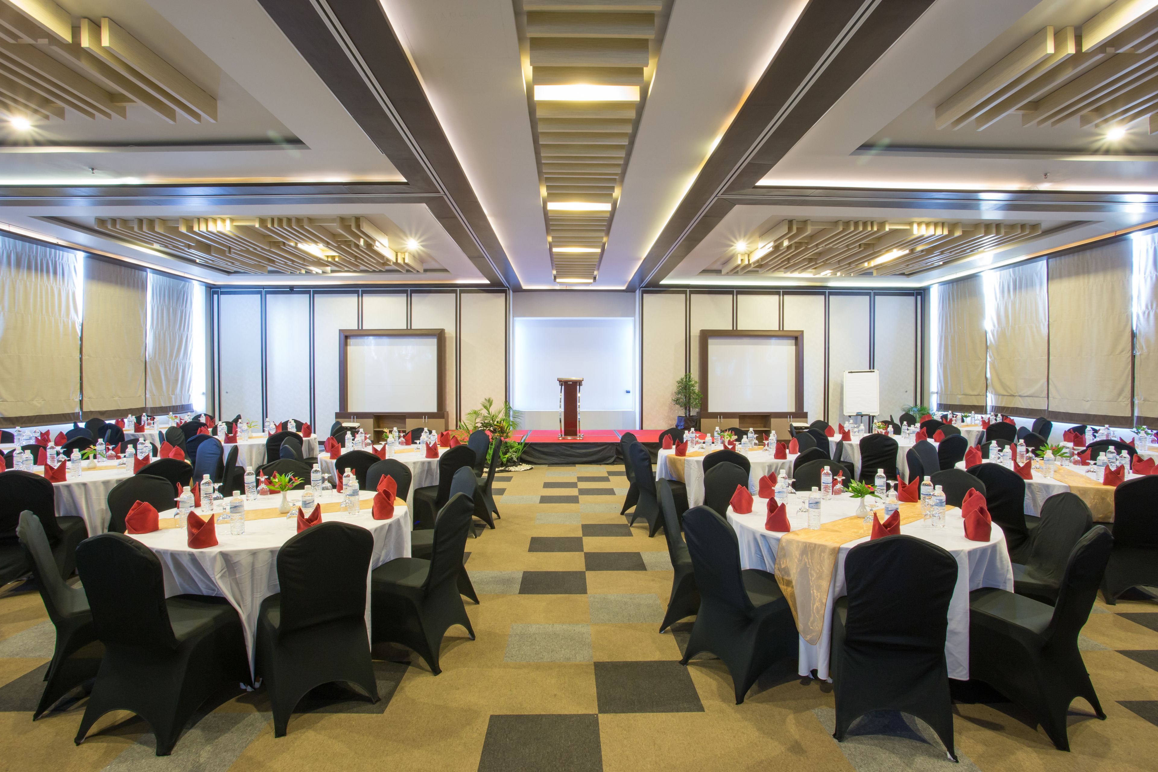 A conference room with round tables, black chairs, and a stage at the front.