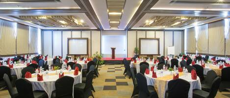 A conference room with round tables, black chairs, and a stage at the front.
