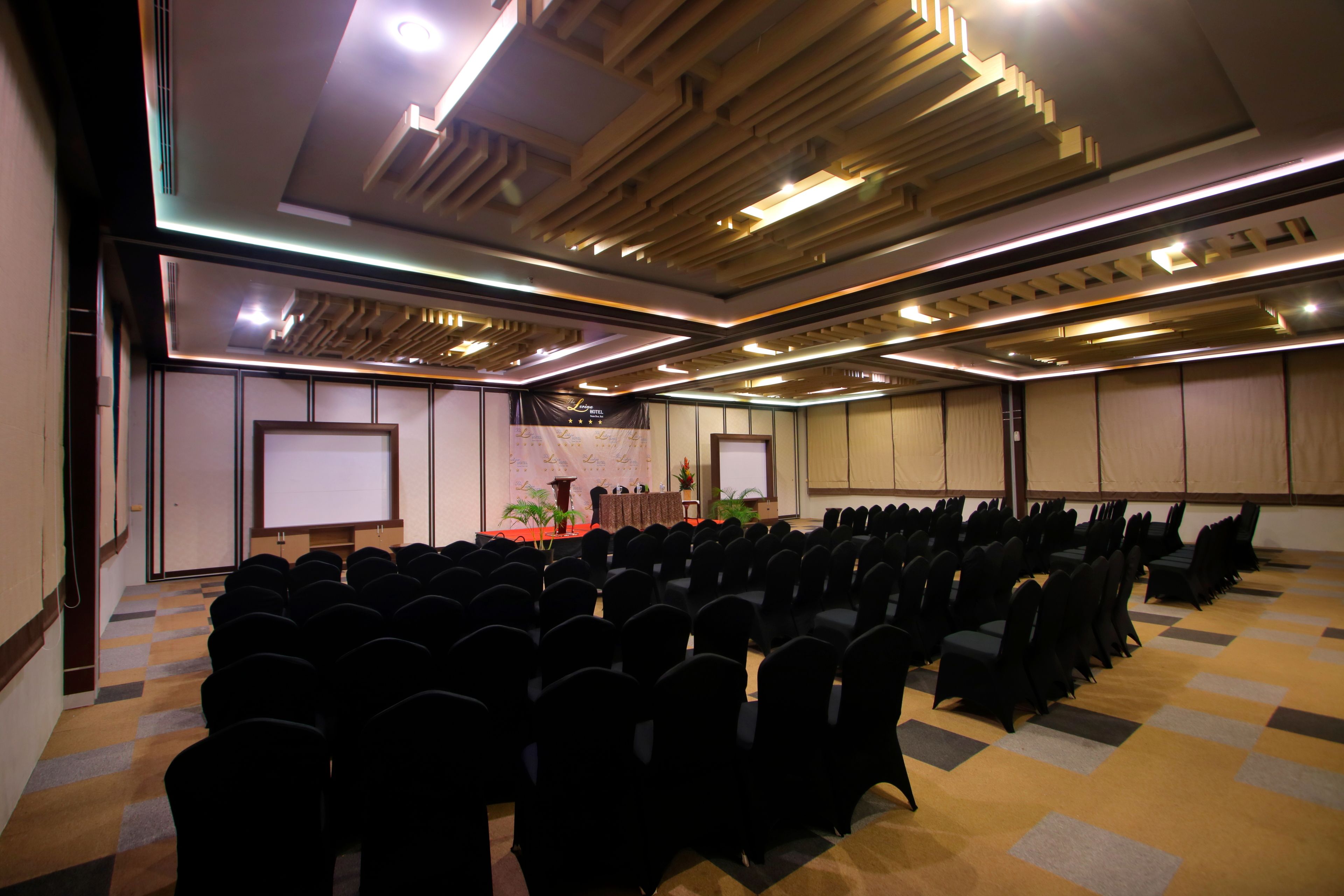 Un salón de conferencias con filas de sillas, un atril y una pantalla de proyector.