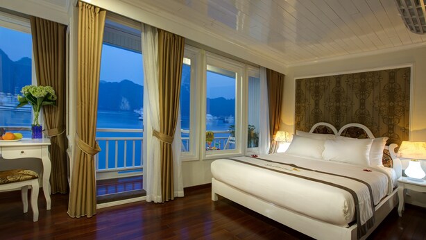 A bedroom with a large bed, a desk, and a view of the sea. - Signature Royal Halong Cruise (Hong Gai)