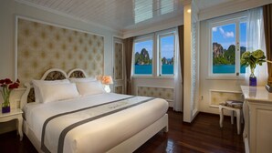 A spacious bedroom with a large bed, a vanity with a mirror, and a view of the sea through a window. - Signature Royal Halong Cruise (Hong Gai)