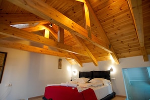 A bedroom with a wooden ceiling, a bed with a red bedspread, and two wall-mounted lights. - Seafalios Villa (Chania)