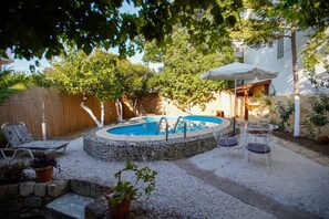 A backyard with a swimming pool, surrounded by a stone wall, a wooden fence, and a covered patio area with chairs and a table. - Seafalios Villa (Chania)
