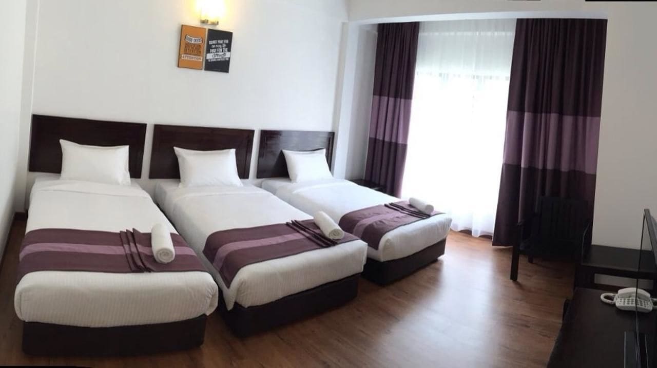 Habitación de hotel con tres camas, piso de madera, un escritorio con teléfono y ventana con cortinas.