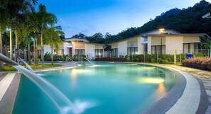 A swimming pool with a water slide, surrounded by modern buildings with a tropical setting.