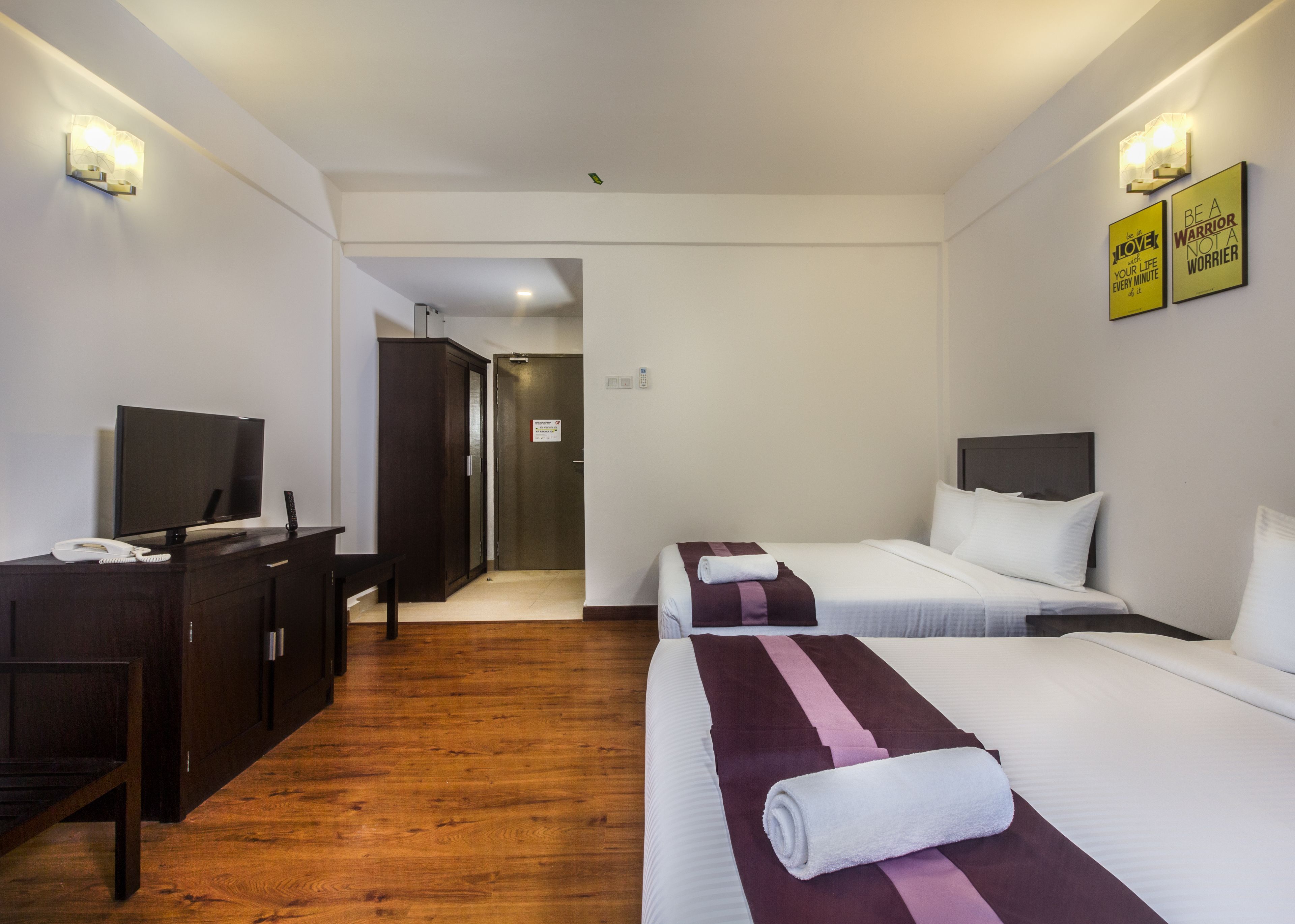 A hotel room with two beds, a desk with a TV, and a wardrobe.