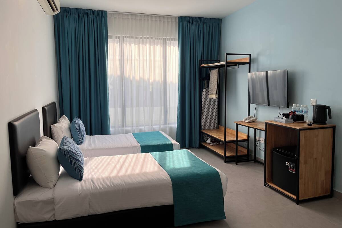 Quarto de hotel com duas camas, uma escrivaninha com televisão, cafeteira e mini-geladeira.
