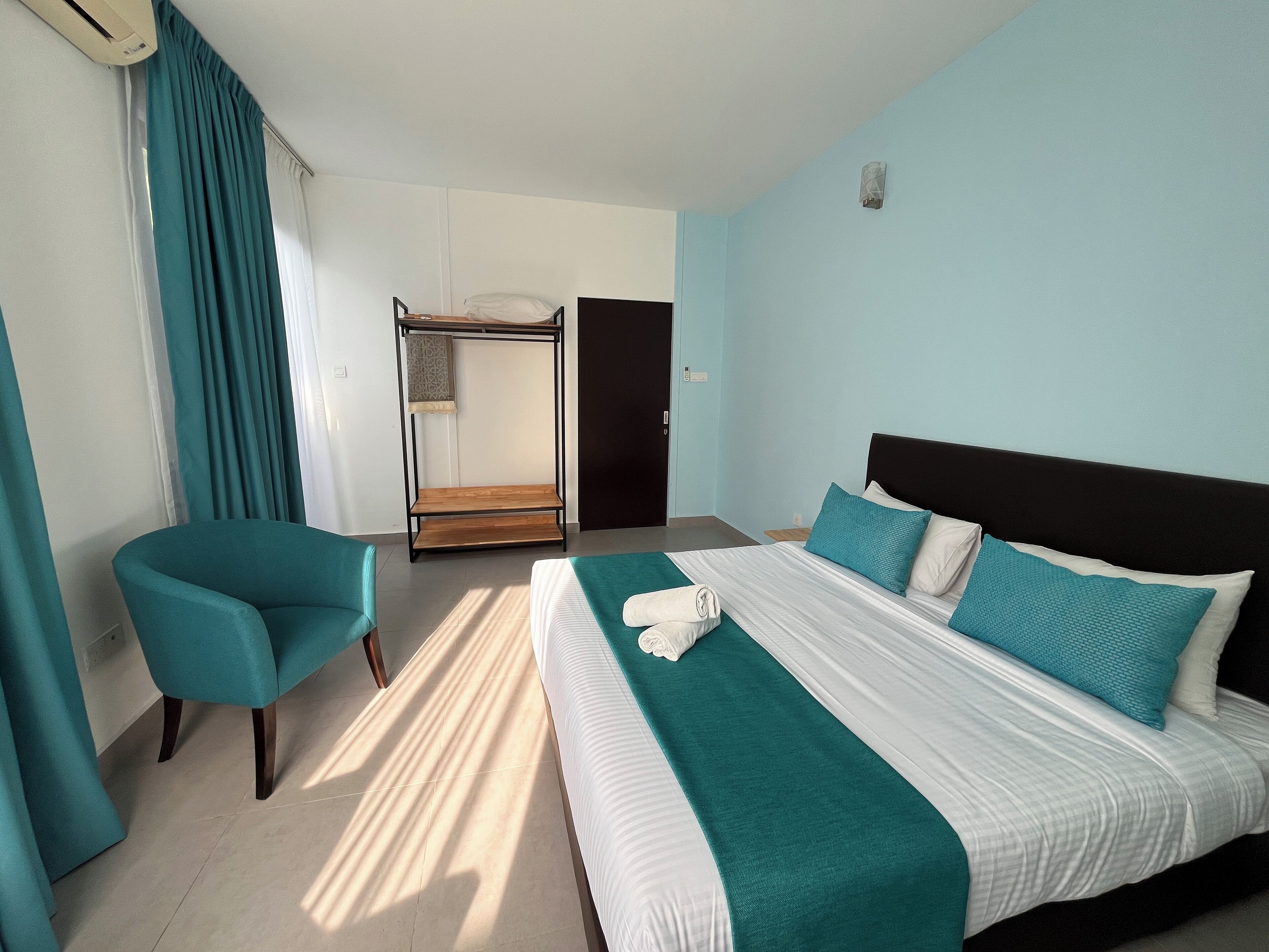 A hotel room with a bed, a chair, a wardrobe, and a window with curtains.