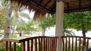 Un balcon abrité offrant une vue sur la plage, les palmiers et un toit de chaume.