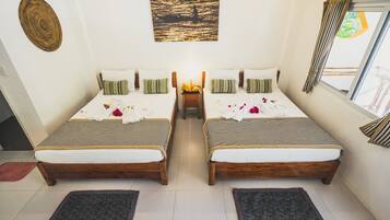 Une chambre double avec deux lits, une petite table sur laquelle se trouve un panier de fruits, et un tableau accroché au mur.
