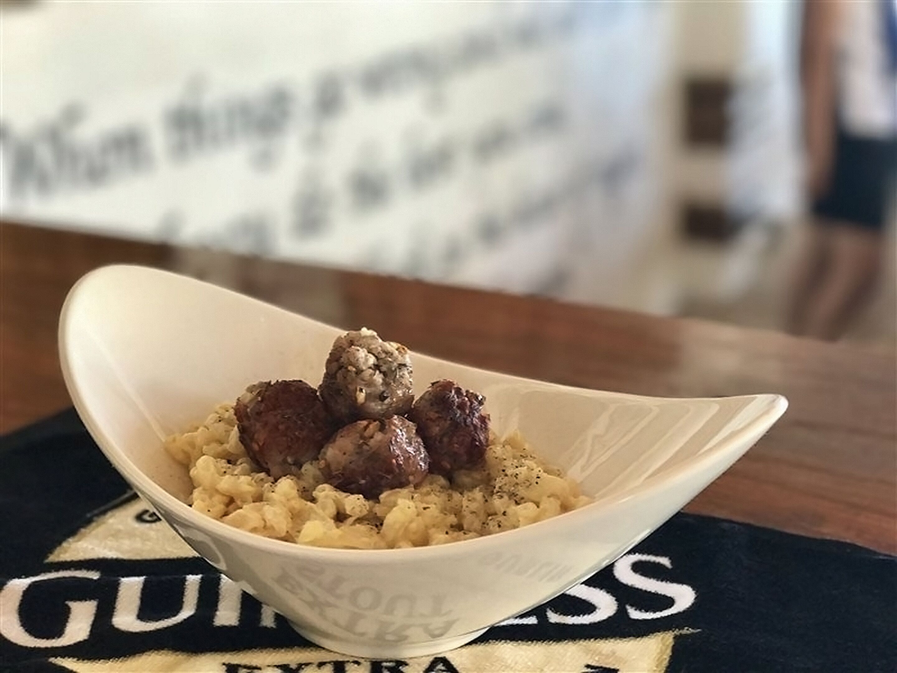 Un bol rempli de nourriture, comprenant des saucisses et une sauce crémeuse, posé sur une table avec un dessous de verre à l’effigie de la marque.