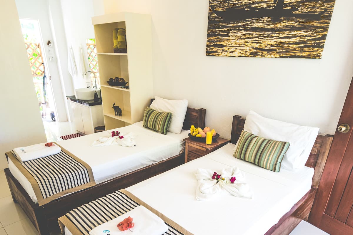 A hotel room with two beds, a bathroom, and a painting of a sunset over water.