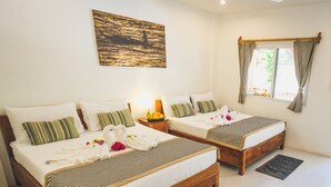 Une chambre d’hôtel avec deux lits en bois, un tableau représentant un coucher de soleil sur l’eau, une fenêtre avec des rideaux et une table de chevet avec une lampe et des fruits.