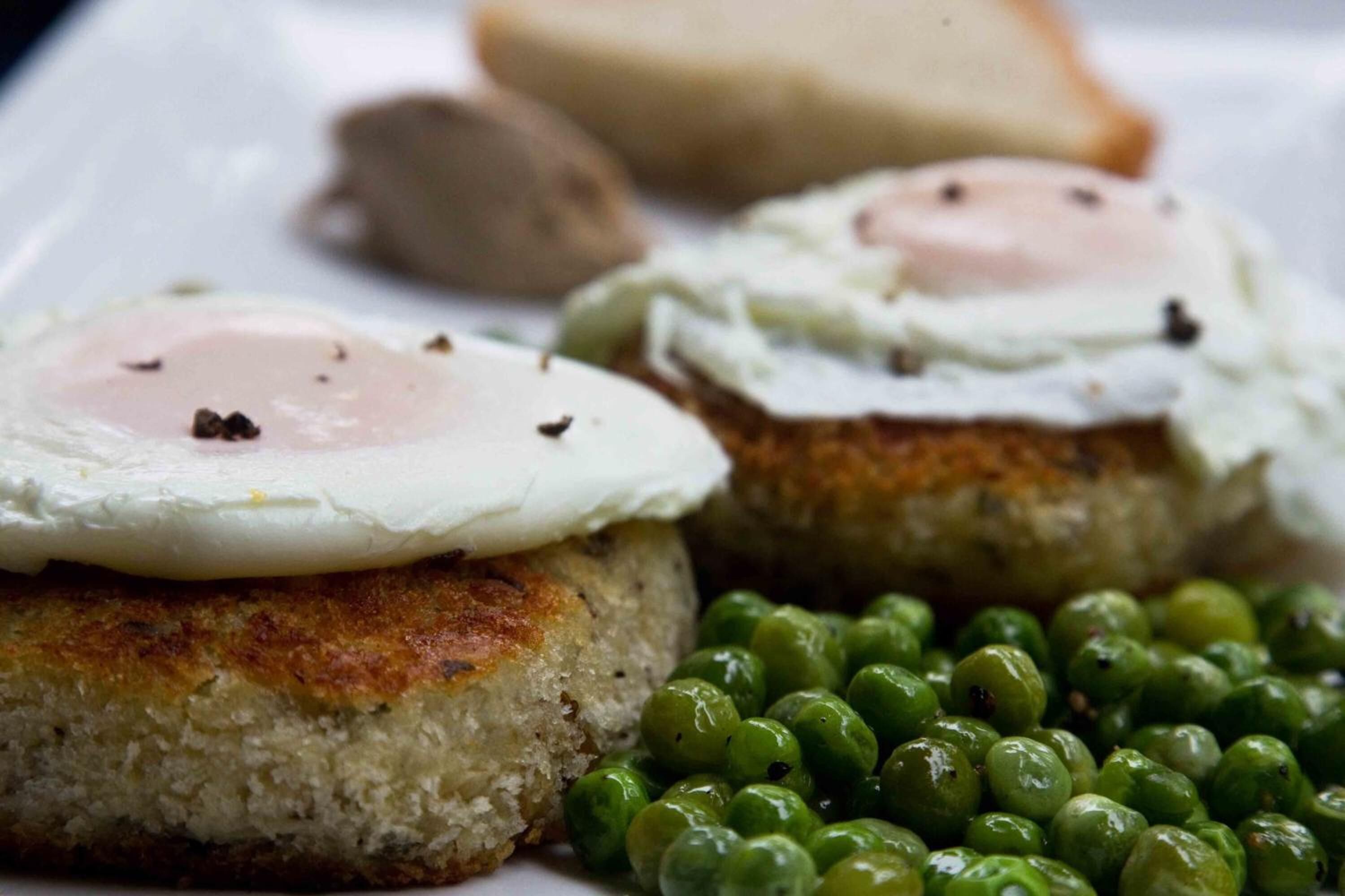 A plate with two fried eggs on cornbread, green peas, and a piece of toast.
