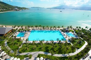 Resort com uma piscina central ampla, rodeada por palmeiras e vista para a praia.