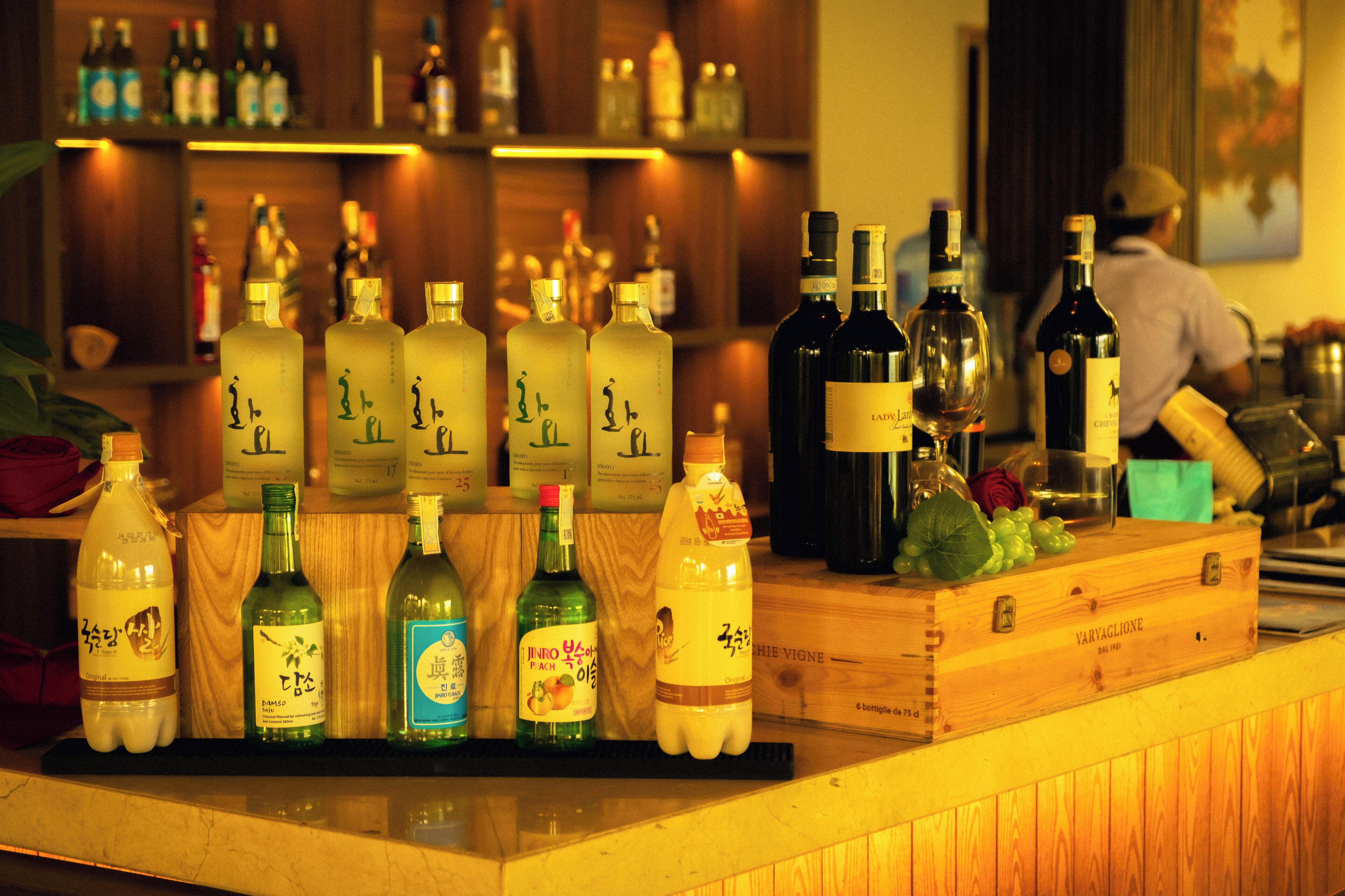 A bar area with various bottles and glasses, wooden shelves, and a counter.