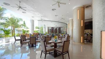 A spacious indoor area with multiple tables and chairs, ceiling fans, and large pillars.