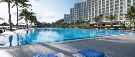 Uma área de piscina de hotel com espreguiçadeiras e um edifício grande ao fundo.