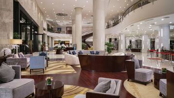 A spacious lobby with multiple seating areas, a central reception desk, and a staircase leading to an upper level.